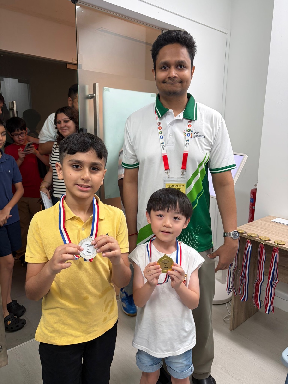 Two young IntChess students proudly holding their tournament medals with their coach