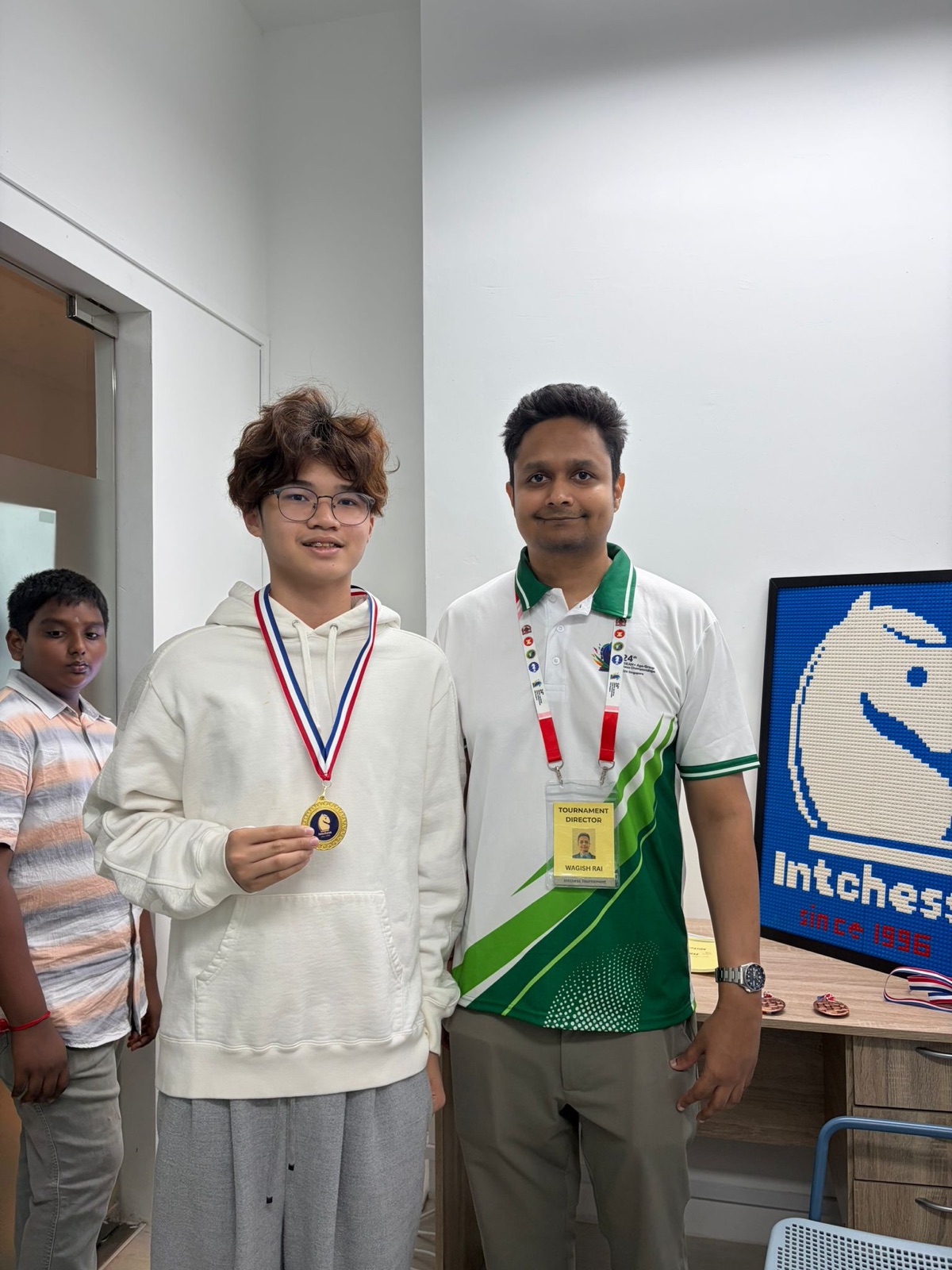 An IntChess student displaying a gold tournament medal beside his coach